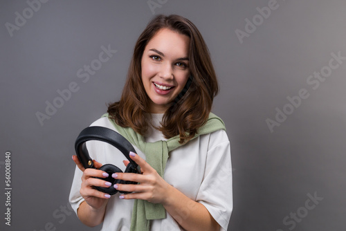 A young smiling woman with headphones on a gray background in the studio. The enjoyment of music. Great mood