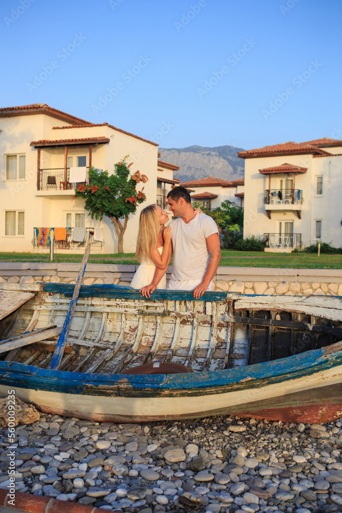 A young couple on the shore near an old wooden boat. Young family on the coast in the resort area