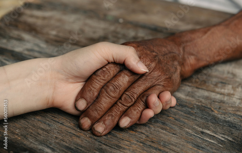 Hands of the old man and a woman hand on the wood table in sun light.