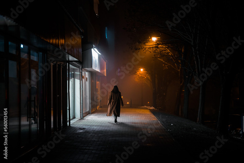 Photographie dark silhouette of a girl dressed in a long coat against the background of a nig