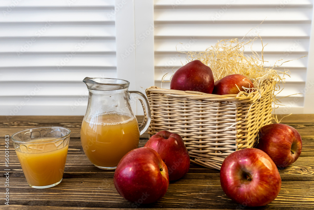 Red apples in a basket and apple juice in a jug on a wooden table Red apples in a basket and apple juice in a jug on a wooden table