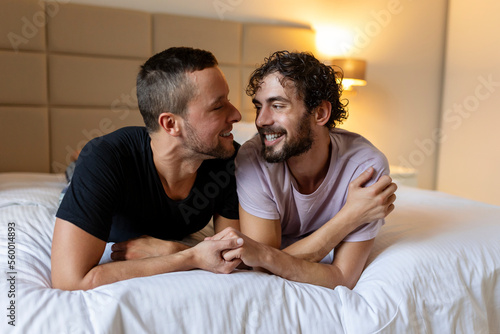 Happy gay couple lying down on the bed at home, hugging and flirting. LGBT gay couple love moments happiness concept © Graphicroyalty