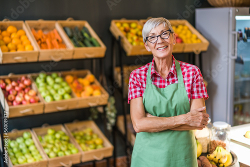 Mature woman works in fruits and vegetables shop. Portrait of small business supermarket owner.