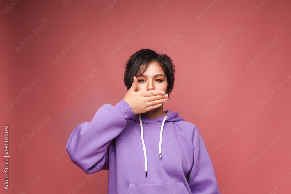 A young woman covers her mouth with her hand on a pink background. a woman with short hair on a pink background A young woman covers her mouth with her hand on a pink background. a woman with short hair on a pink background