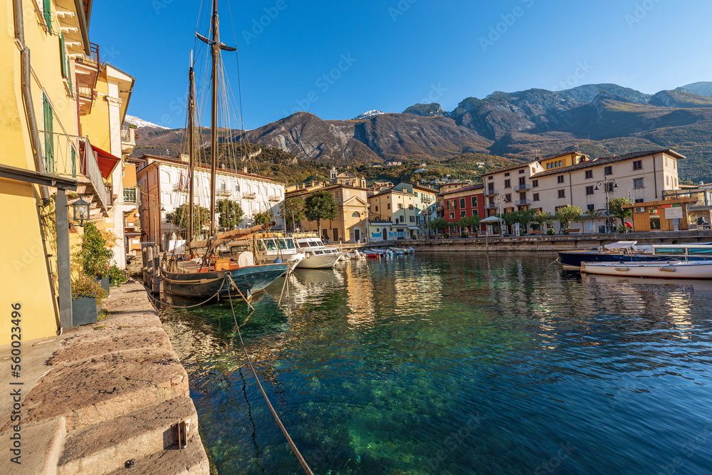 Small port of Malcesine village with small boats moored. Famous tourist resort on the coast of Lake Garda (Lago di Garda). Verona province, Veneto, Italy, Europe. Mountain range of Monte Baldo.