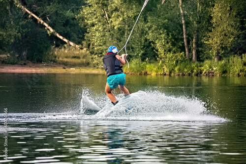 A young woman wakeboarding on a lake on summer day in a life jacket. Soft focus. Action blur.