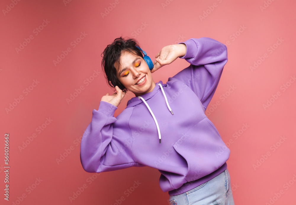 young brunette girl in a lilac sweater and headphones poses in isolation on a pink background in the studio. The concept of people's lifestyle.Listen to music with headphones, dance. studio portrait. young brunette girl in a lilac sweater and headphones poses in isolation on a pink background in the studio. The concept of people's lifestyle.Listen to music with headphones, dance. studio portrait.