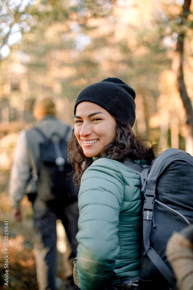 Happy woman looking over shoulder while hiking in forest Happy woman looking over shoulder while hiking in forest