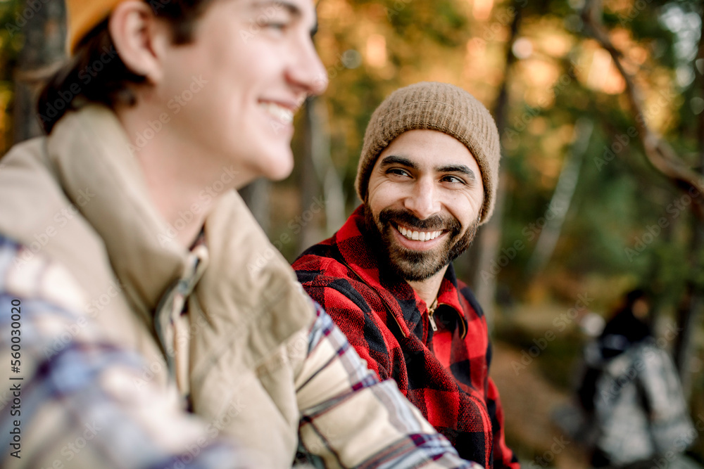 Happy man wearing plaid shirt talking to male friend during camping Happy man wearing plaid shirt talking to male friend during camping