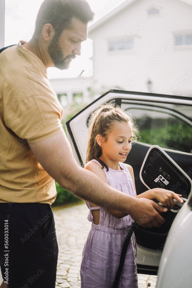 Girl learning to charge electric car while standing by father Girl learning to charge electric car while standing by father