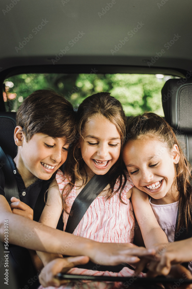 Happy siblings sharing tablet PC while while traveling in car Happy siblings sharing tablet PC while while traveling in car