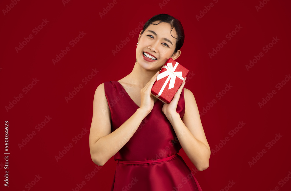 Young asian woman in red luxury dress holding and giving present red box white bow pose looking and smiling red background. Young asian woman in red luxury dress holding and giving present red box white bow pose looking and smiling red background.