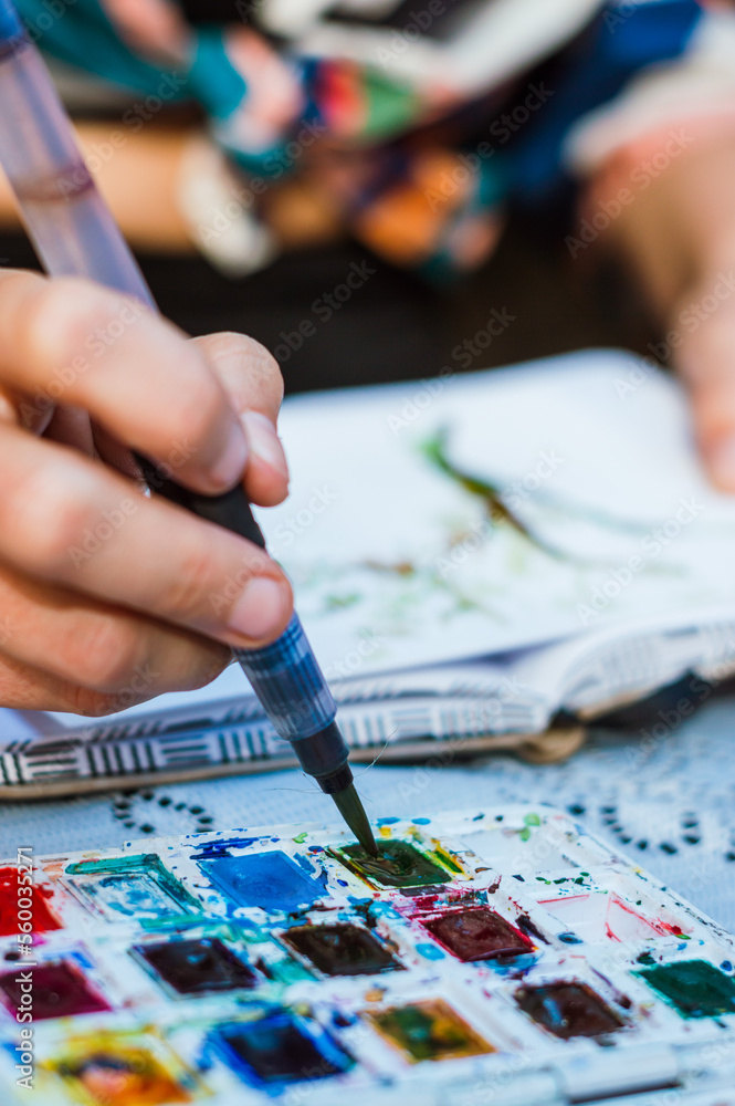 vertical image of detail of woman dipping the brush in watercolor, making a drawing. vertical image of detail of woman dipping the brush in watercolor, making a drawing.