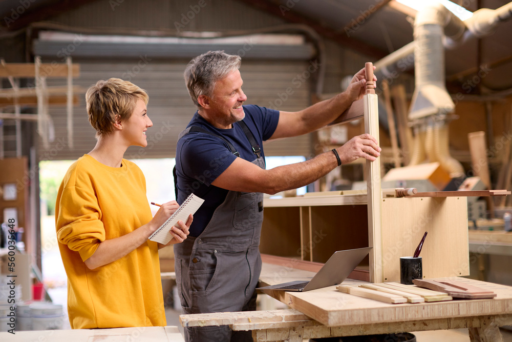 Female Apprentice Learning Skills From Mature Male Carpenter In Furniture Workshop Female Apprentice Learning Skills From Mature Male Carpenter In Furniture Workshop