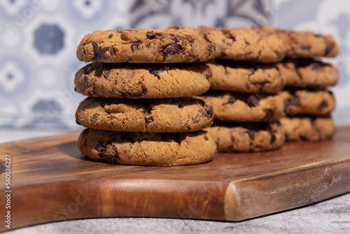 Homemade chocolate chip cookies stacked on a wooden chopping board. With a blue tile background