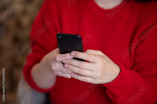 Black phone in women's hands in a red sweater