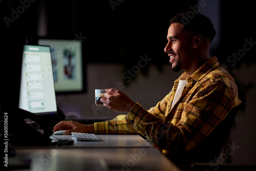 Businessman Working Late In Office With Face Illuminated By Computer Screen Drinking Coffee