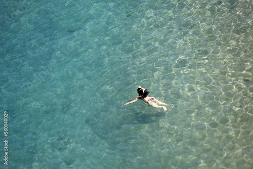 Aerial view to azure sea and woman swimming in transparent water. Girl swimmer, beach vacation