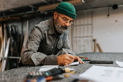 Bearded male entrepreneur wearing eyeglasses while writing at workbench photo