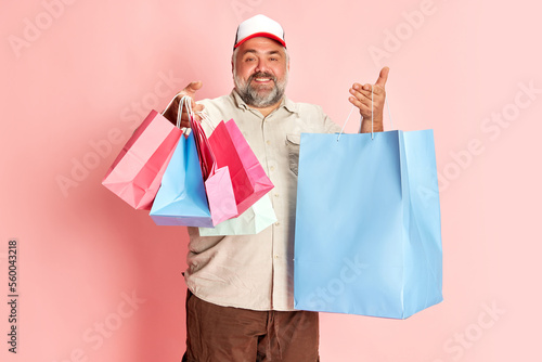 Portrait of mature man in casual clothes going shopping, posing with shopping trolley over pink studio background. Good sales