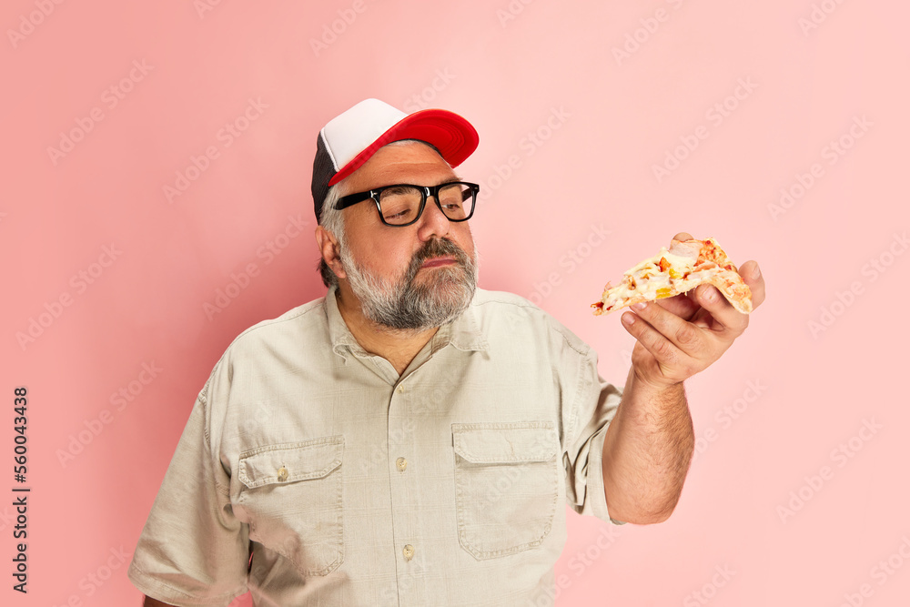 Portrait of mature man in casual clothes eating delicious Italian pizza over pink studio background Portrait of mature man in casual clothes eating delicious Italian pizza over pink studio background