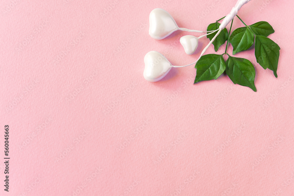 White hearts and green fresh leaves. Beautiful romantic composition on a delicate pink paper background.