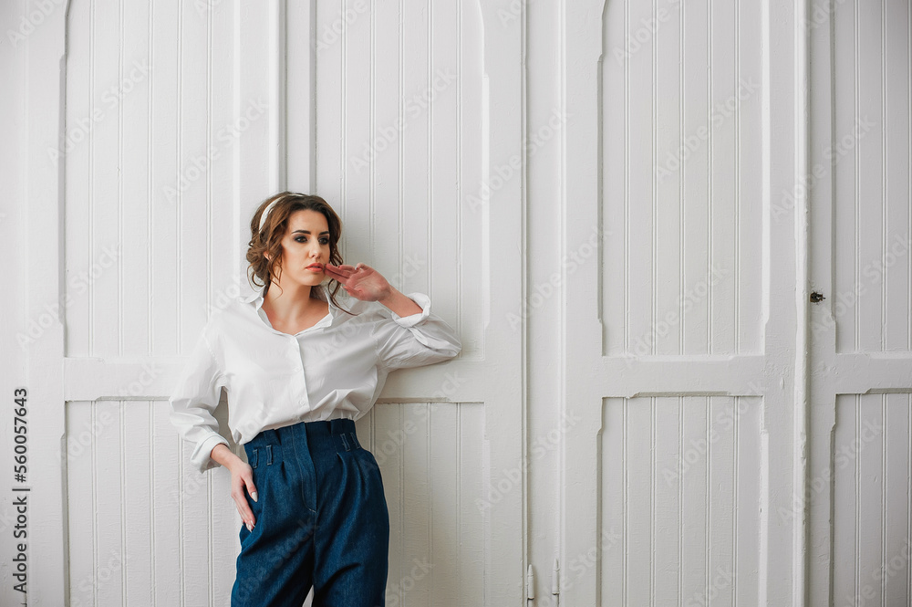 a sexy girl dressed in a white shirt and jeans poses indoors in front of a white door; a sexy girl dressed in a white shirt and jeans poses indoors in front of a white door;