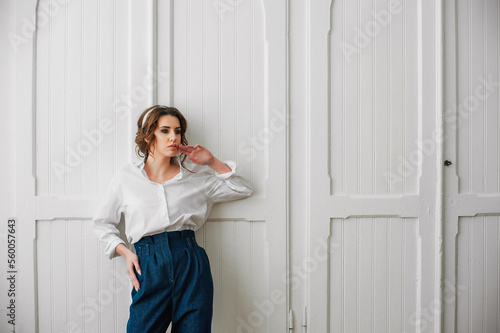 a sexy girl dressed in a white shirt and jeans poses indoors in front of a white door;