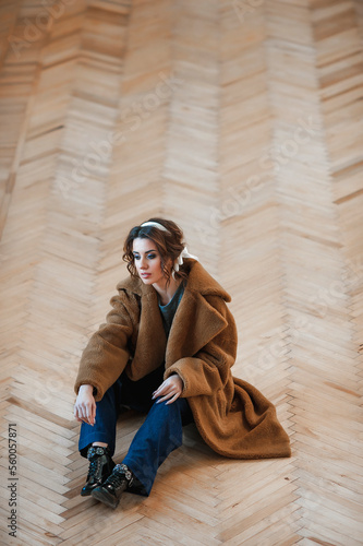 sexy girl dressed in a fur coat posing indoors sitting on the floor; warm long fur coat