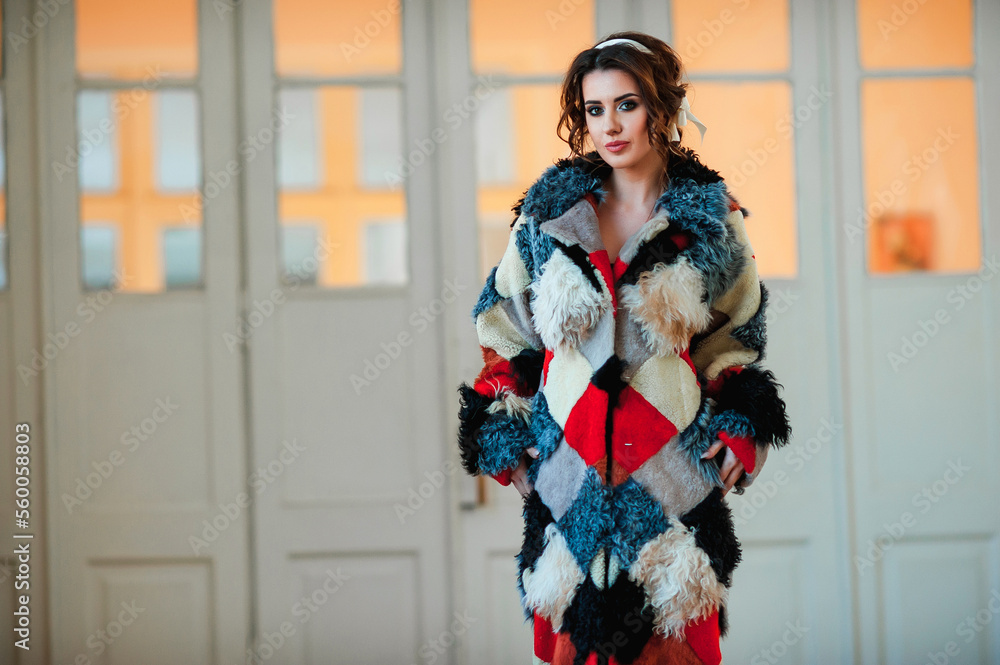  sexy girl dressed in a fur coat and posing indoors on the background of the door; warm long fur coat