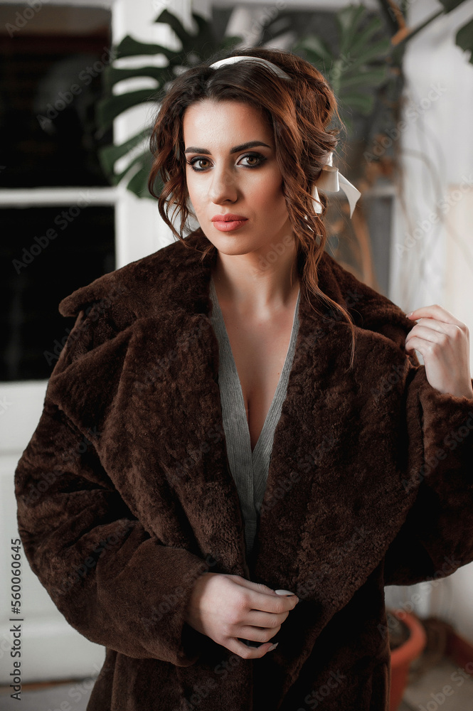 sexy girl dressed in a fur coat and posing indoors on the background of the door; warm long fur coat sexy girl dressed in a fur coat and posing indoors on the background of the door; warm long fur coat