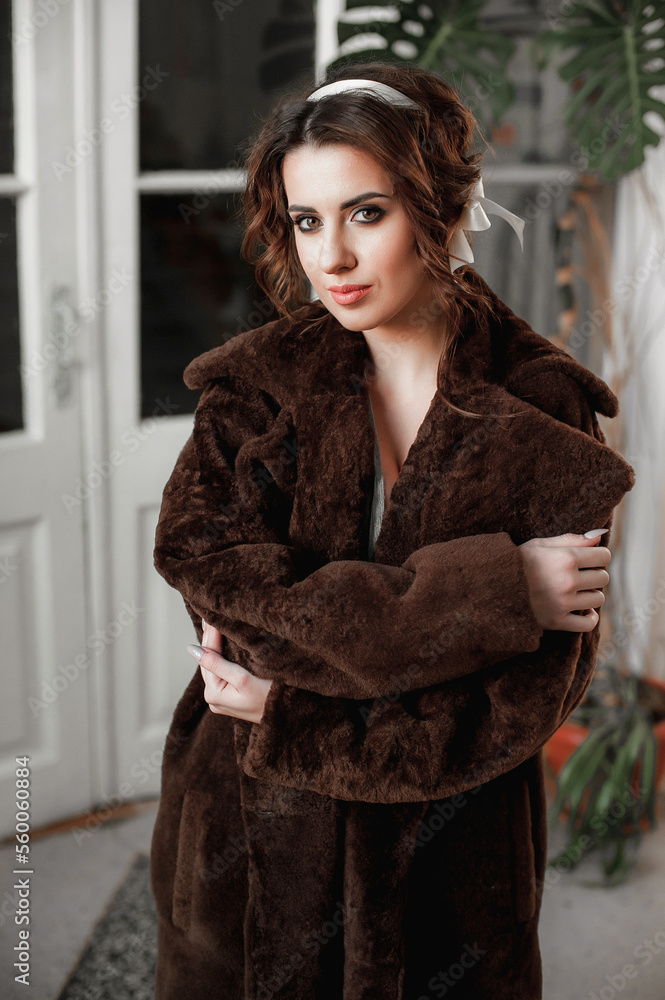 sexy girl dressed in a fur coat and posing indoors on the background of the door; warm long fur coat sexy girl dressed in a fur coat and posing indoors on the background of the door; warm long fur coat