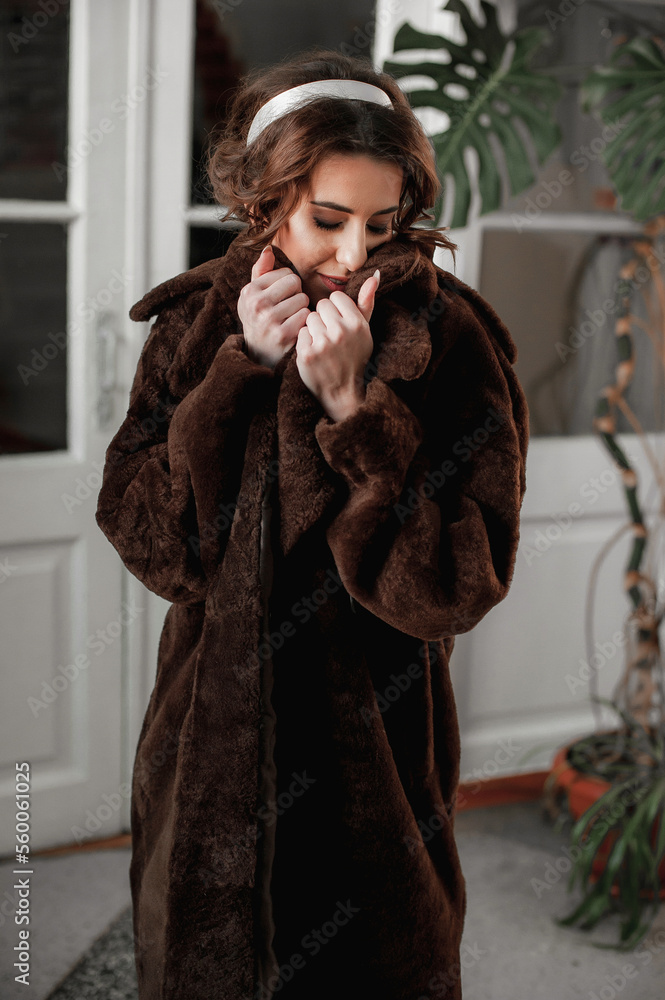 sexy girl dressed in a fur coat and posing indoors on the background of the door; warm long fur coat sexy girl dressed in a fur coat and posing indoors on the background of the door; warm long fur coat