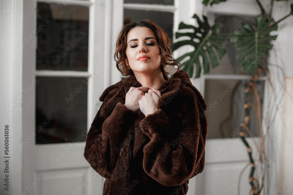 sexy girl dressed in a fur coat and posing indoors on the background of the door; warm long fur coat sexy girl dressed in a fur coat and posing indoors on the background of the door; warm long fur coat