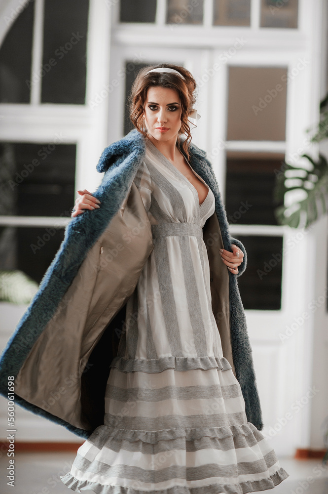 Fototapeta premium sexy girl dressed in a fur coat and posing indoors on the background of the door; warm long fur coat