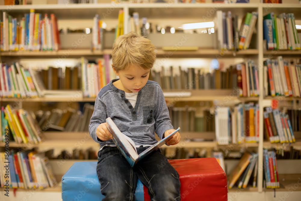 Adorable little boy, sitting in library, reading book and choosing what to lend, kid in book store. Adorable little boy, sitting in library, reading book and choosing what to lend, kid in book store.