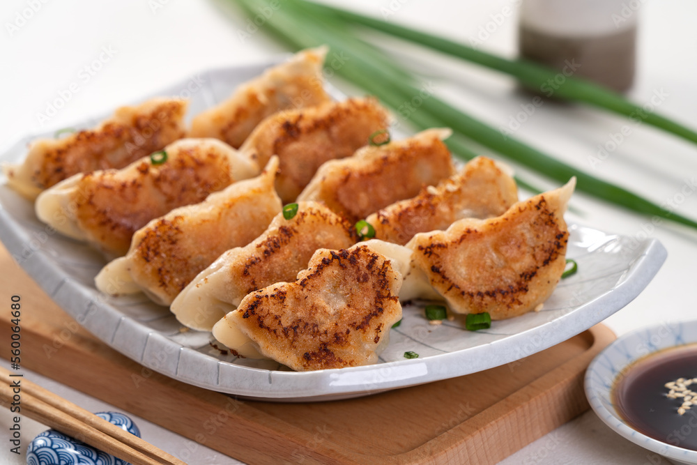 Pan-fried gyoza dumpling jiaozi in a plate with soy sauce on white table background. Pan-fried gyoza dumpling jiaozi in a plate with soy sauce on white table background.