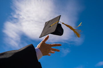 Close-up of a woman's hand with a graduation cap against the blue sky. 