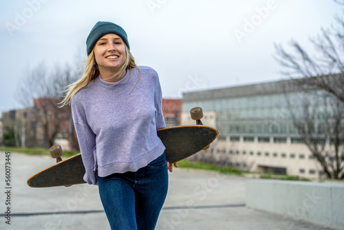 Young woman with skateboard walking smiling in urban environment, trendy teenager of generation z