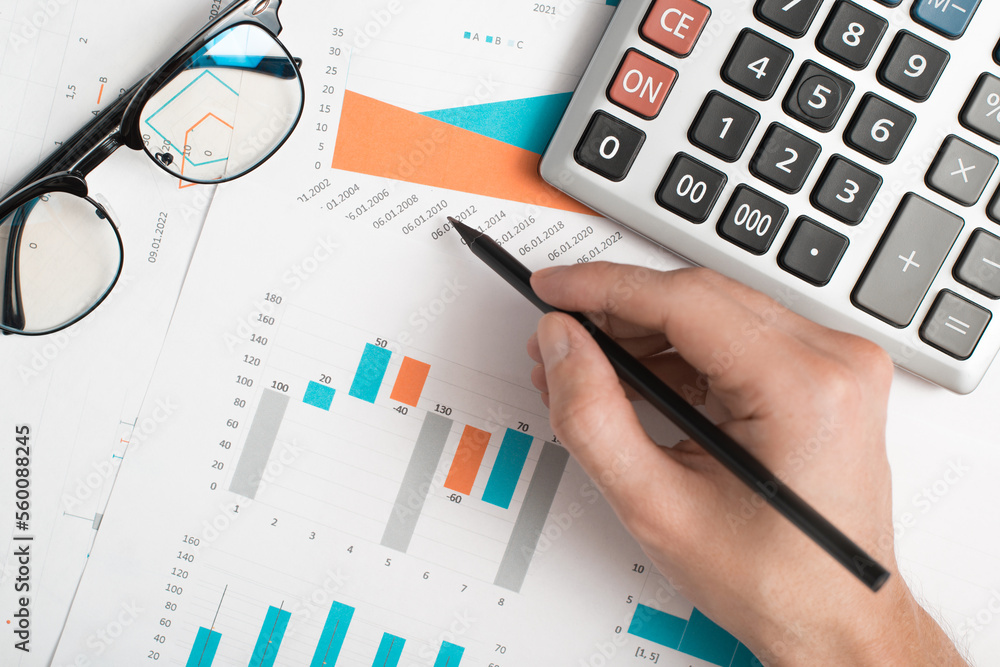 Financial work, accountant, research of economic indicators, document analytics. Top view hand of businessman using graphs and charts at workplace, close-up Financial work, accountant, research of economic indicators, document analytics. Top view hand of businessman using graphs and charts at workplace, close-up