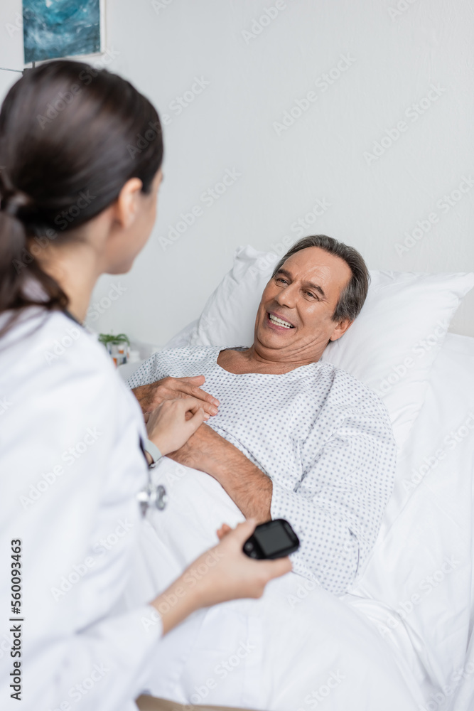 Smiling senior patient looking at blurred doctor with glucometer in clinic. Smiling senior patient looking at blurred doctor with glucometer in clinic.