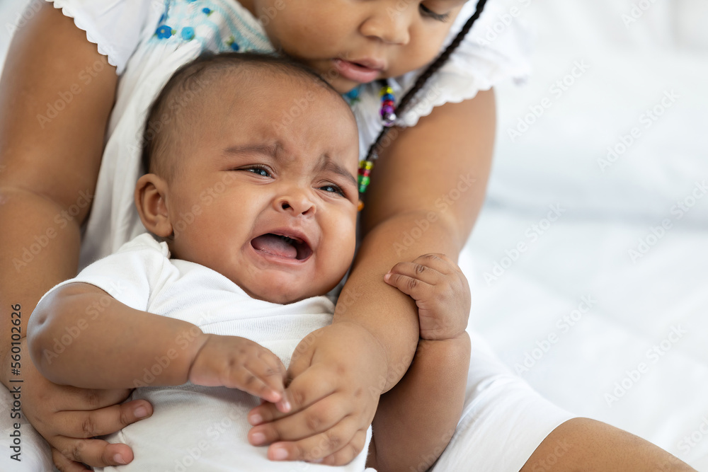 African newborn baby crying and her sister soothing to stop crying on bed African newborn baby crying and her sister soothing to stop crying on bed