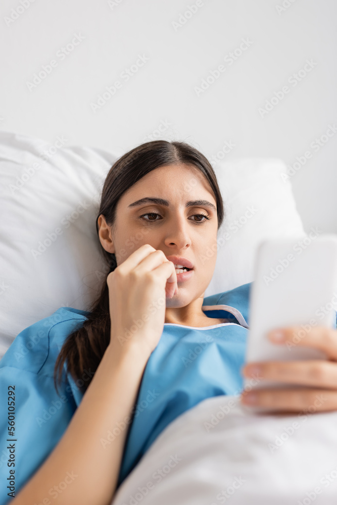 Stressed patient using smartphone while lying on bed in hospital ward. Stressed patient using smartphone while lying on bed in hospital ward.