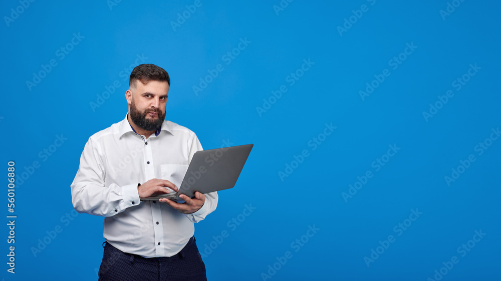 A bearded man holds a laptop in his hands on a blue background. A solid man in a white shirt works at a laptop and looks into the camera.