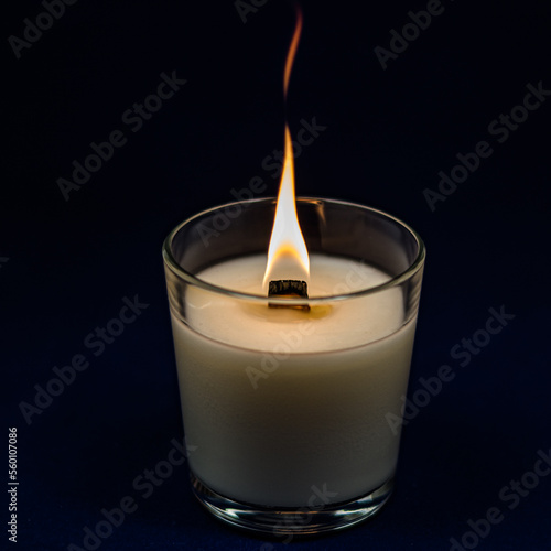 A candle in a candlestick on a dark background. A bright-burning candle on a black background.