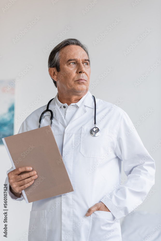 Senior doctor holding paper folder and looking away in clinic. Senior doctor holding paper folder and looking away in clinic.