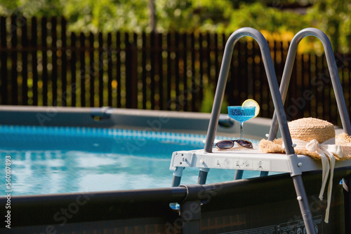 A glass of delicious blue cocktail Blue Lagoon and yellow lemons on the background of the pool. Alcoholic cocktail juicy fruit blue with curacao liqueur, ice cubes and a slice of lemon.