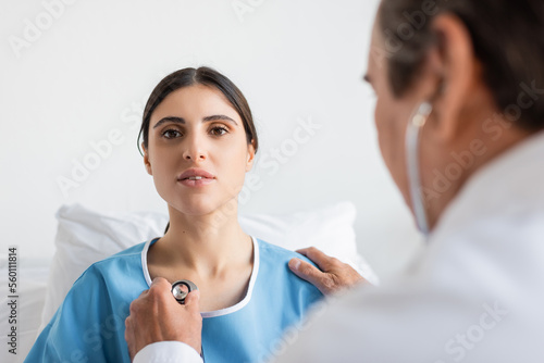 Blurred doctor holding stethoscope near chest of patient in clinic.