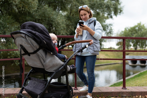 young mother with a baby stroller on a walk in the park with a phone in her hands