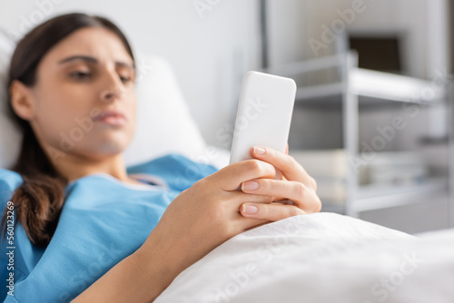 Blurred patient using mobile phone while lying on hospital bed.